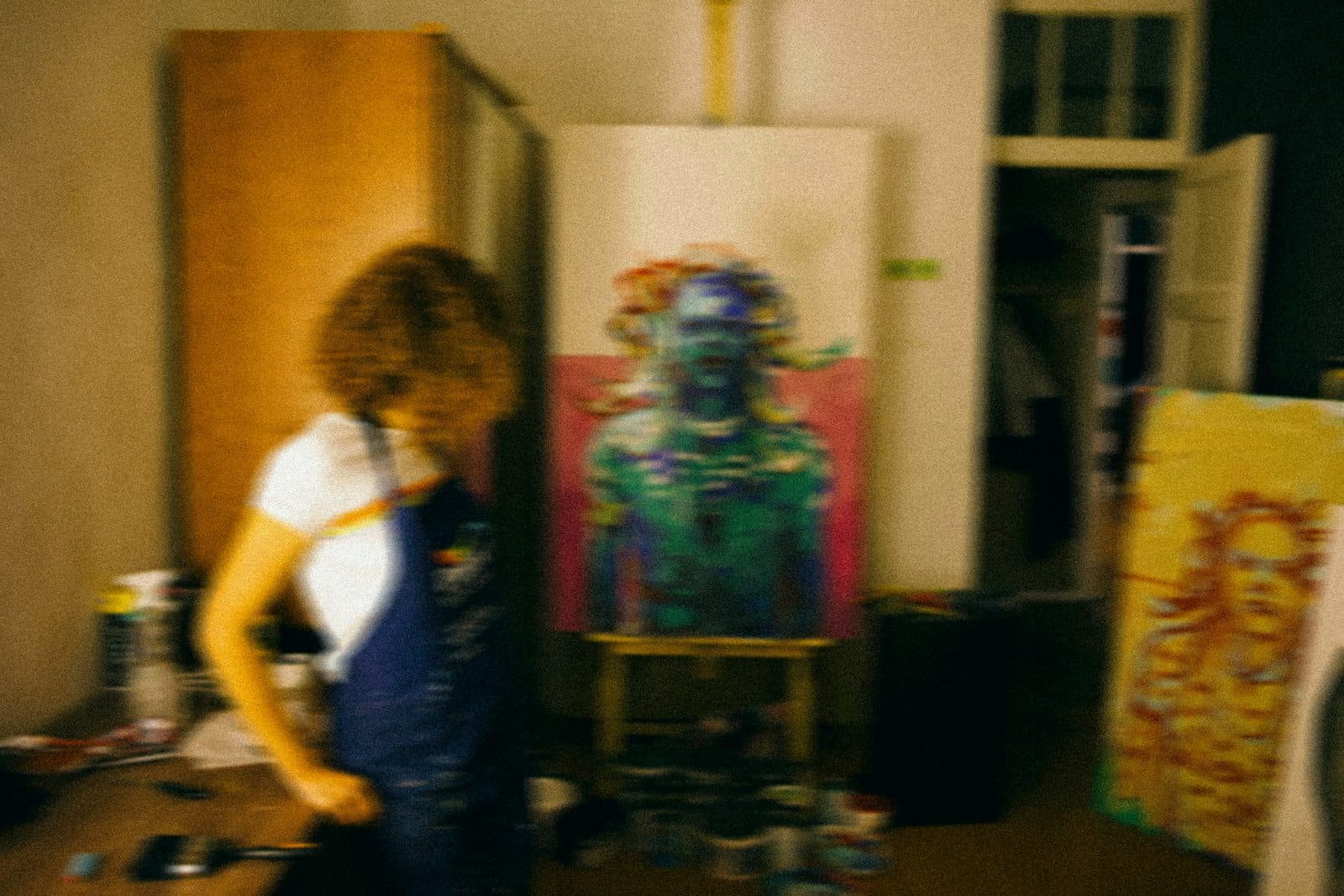 A painter working at an easel in a studio, caught mid-movement.